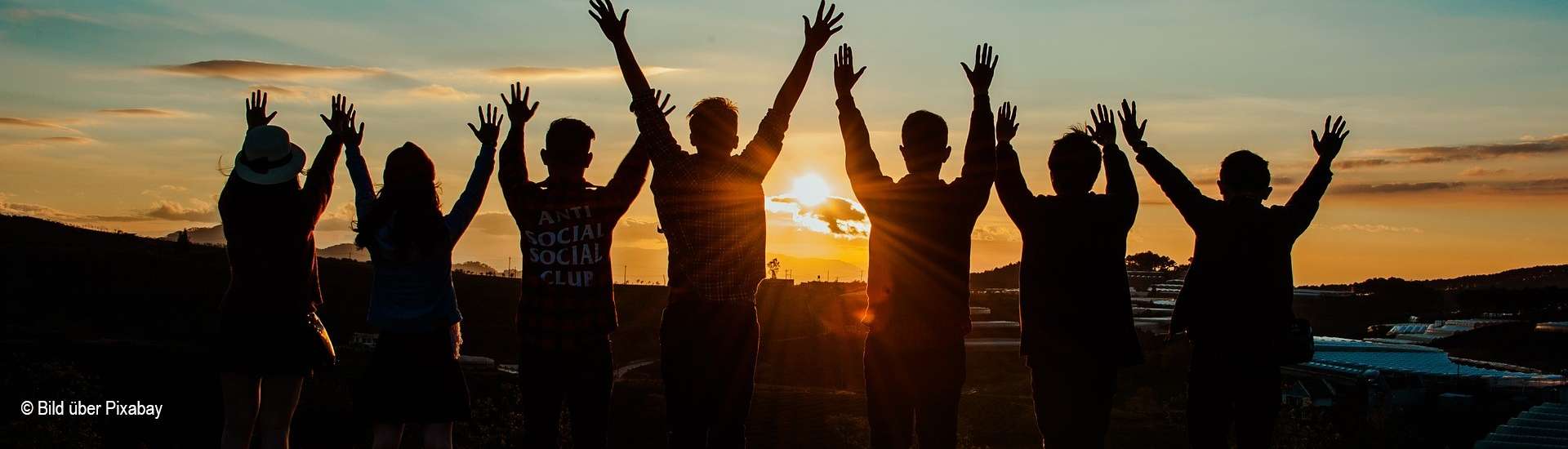 Bei Sonnenuntergang strecken sieben junge Menschen ihre Arme in die Luft